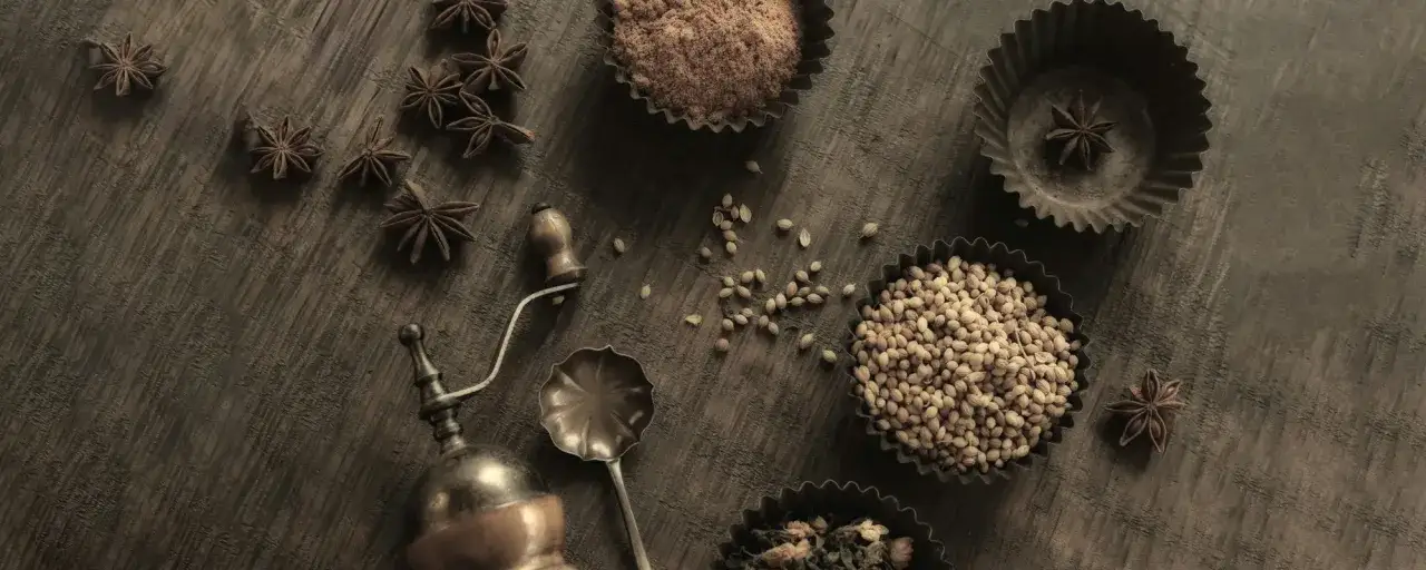 Gwiazdki anyżu, nasiona kolendry i mielony cynamon na drewnianym blacie. Stara młynek do przypraw i łyżka dodają oriental essence.