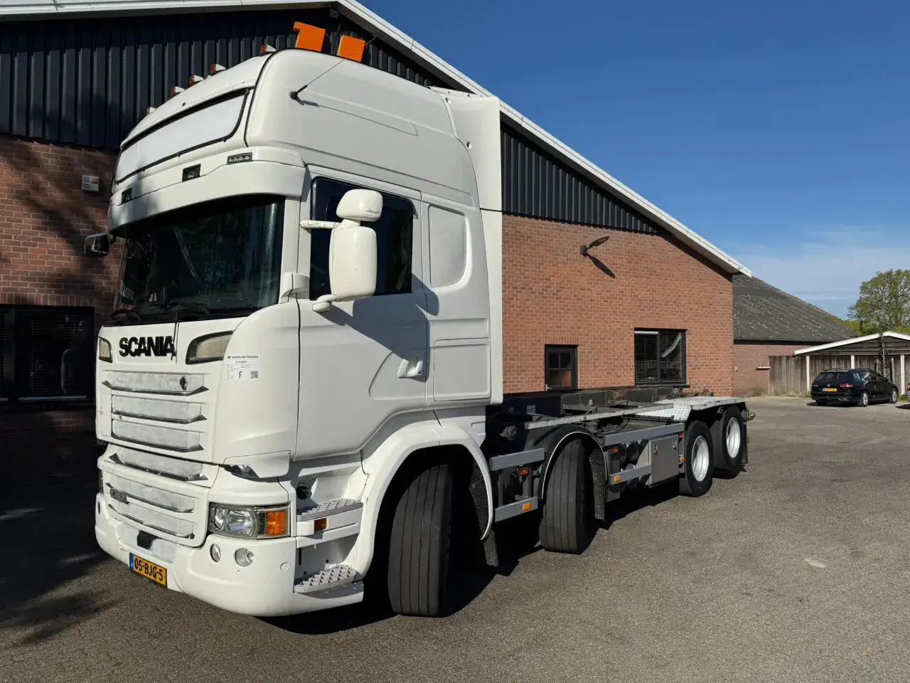 Un camion blanc de la gamme Scania, pr&ecirc;t pour le transport, stationn&eacute; devant un b&acirc;timent.