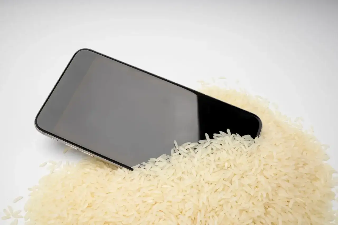 Czarny iPhone zanurzony w ryżu, sugerujący próbę osuszenia po zalaniu. Wykryto ciecz iPhone.