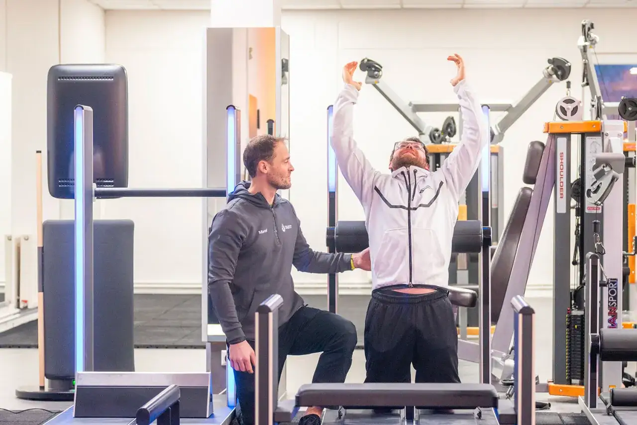 Ein Trainer unterst&uuml;tzt einen Mann beim Training in einem modernen Fitnessstudio. Vielleicht eine der vielen spannenden **Igersheim Veranstaltungen** im Bereich Gesundheit.