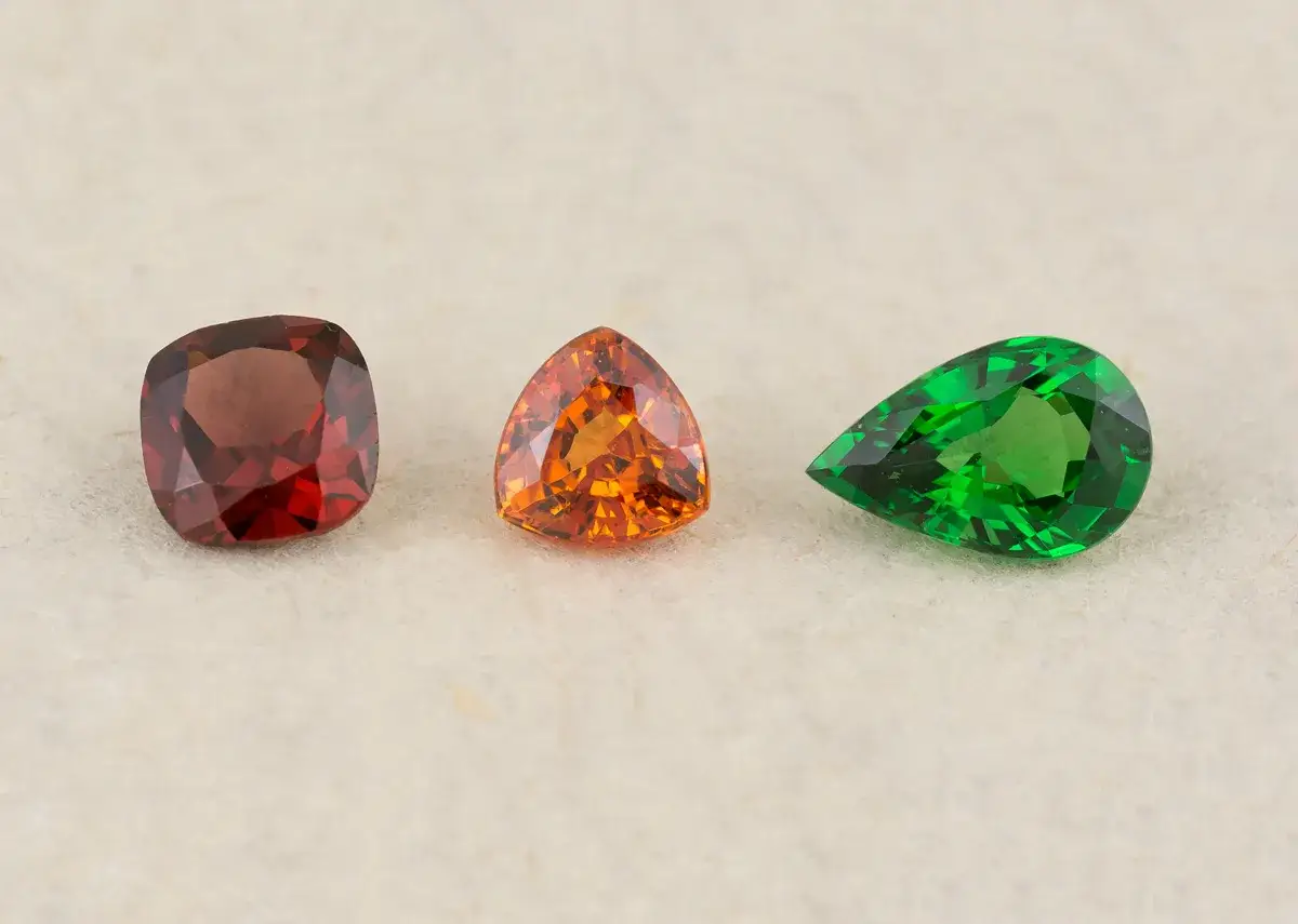 Tres gemas facetadas: una granate rojiza, una naranja triangular y una esmeralda verde en forma de pera. La piedra enero, el granate, inspira esta colección.
