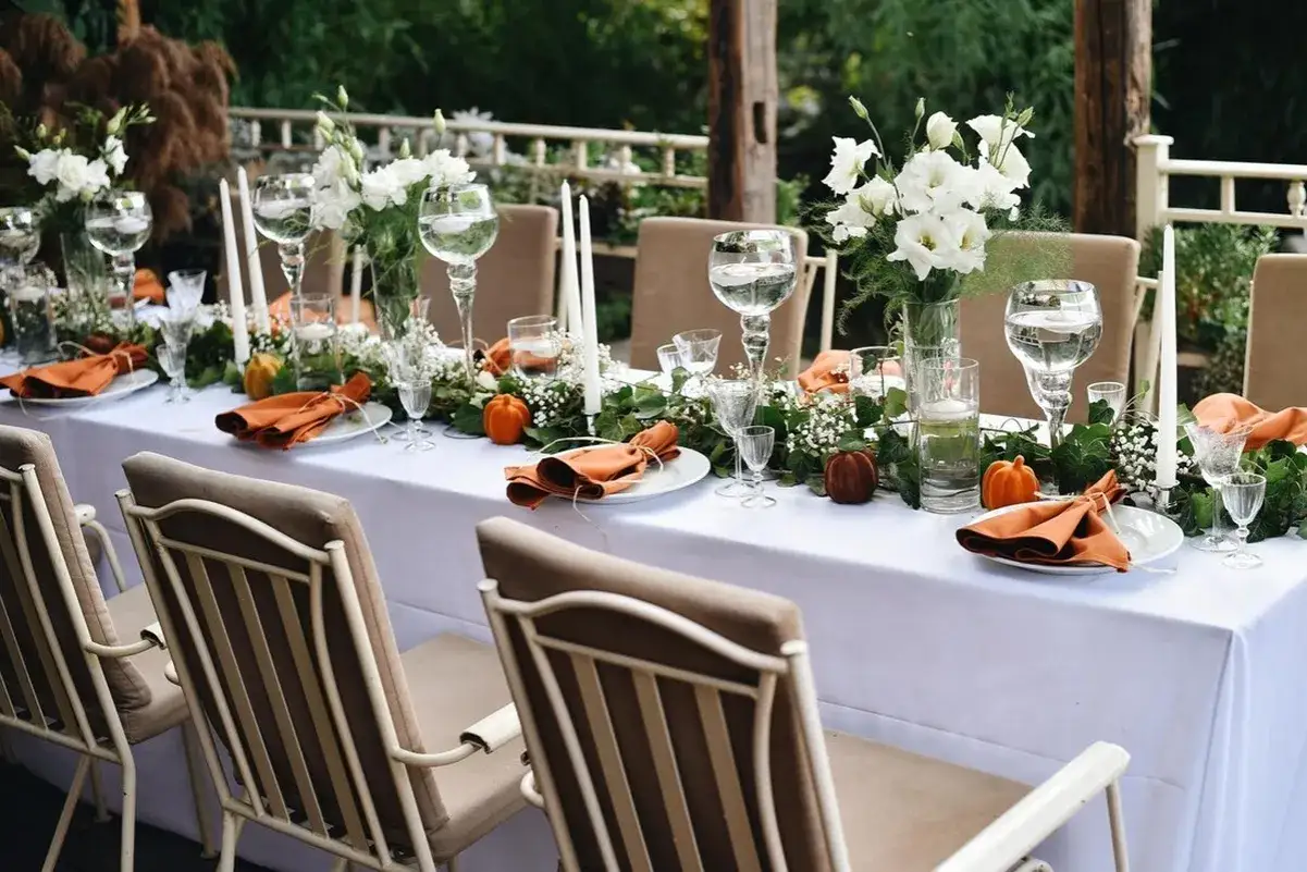 Elegancko nakryty stół na przyjęcie, z pomarańczowymi serwetkami i dyniami. Zastanawiasz się, ile trwa komunia? To zależy od wielu czynników, ale zazwyczaj jest to uroczystość rodzinna.