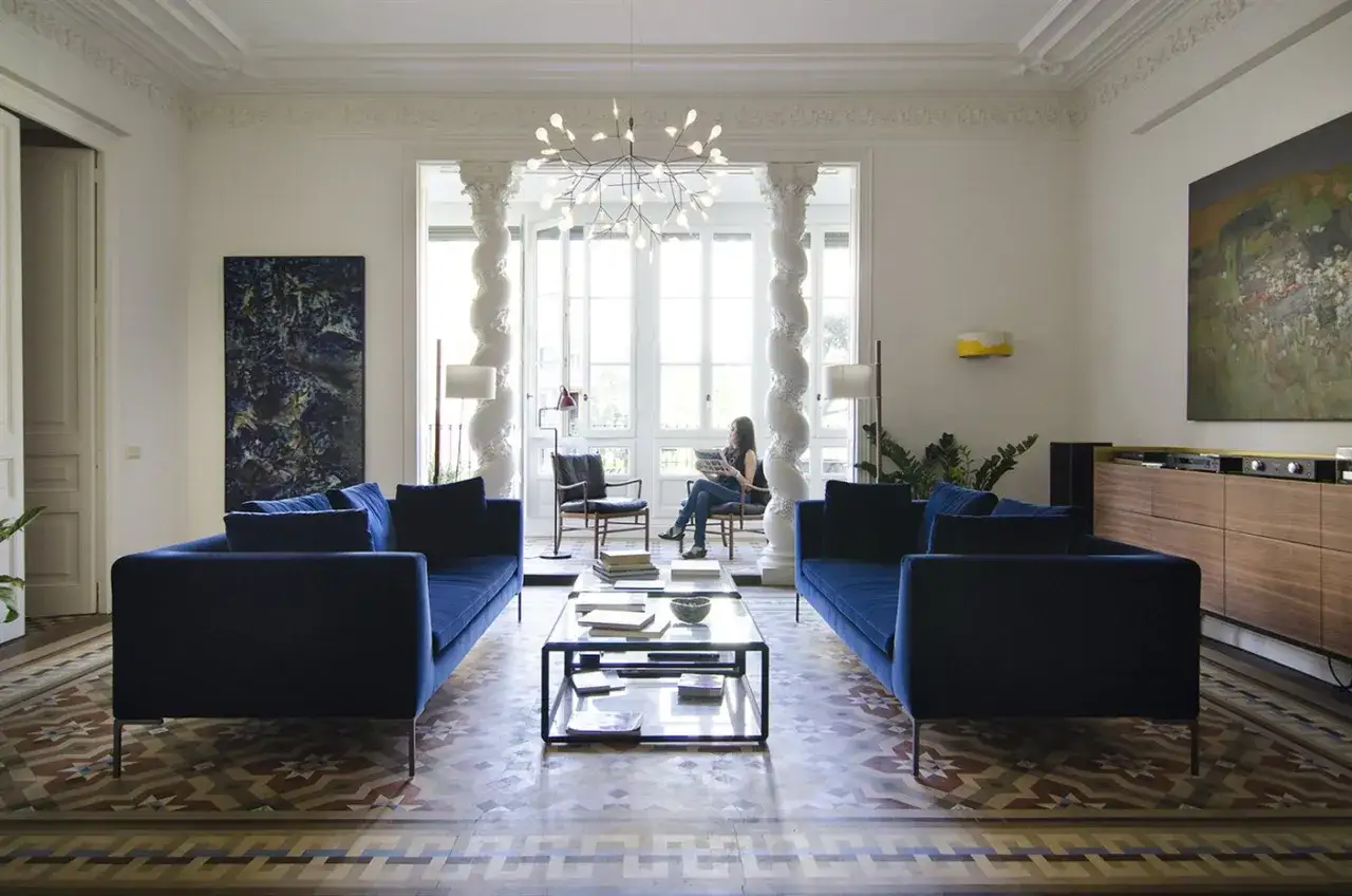 Ideas para decorar una columna en el sal&oacute;n: dos sof&aacute;s azules flanquean una chimenea con una mujer leyendo.