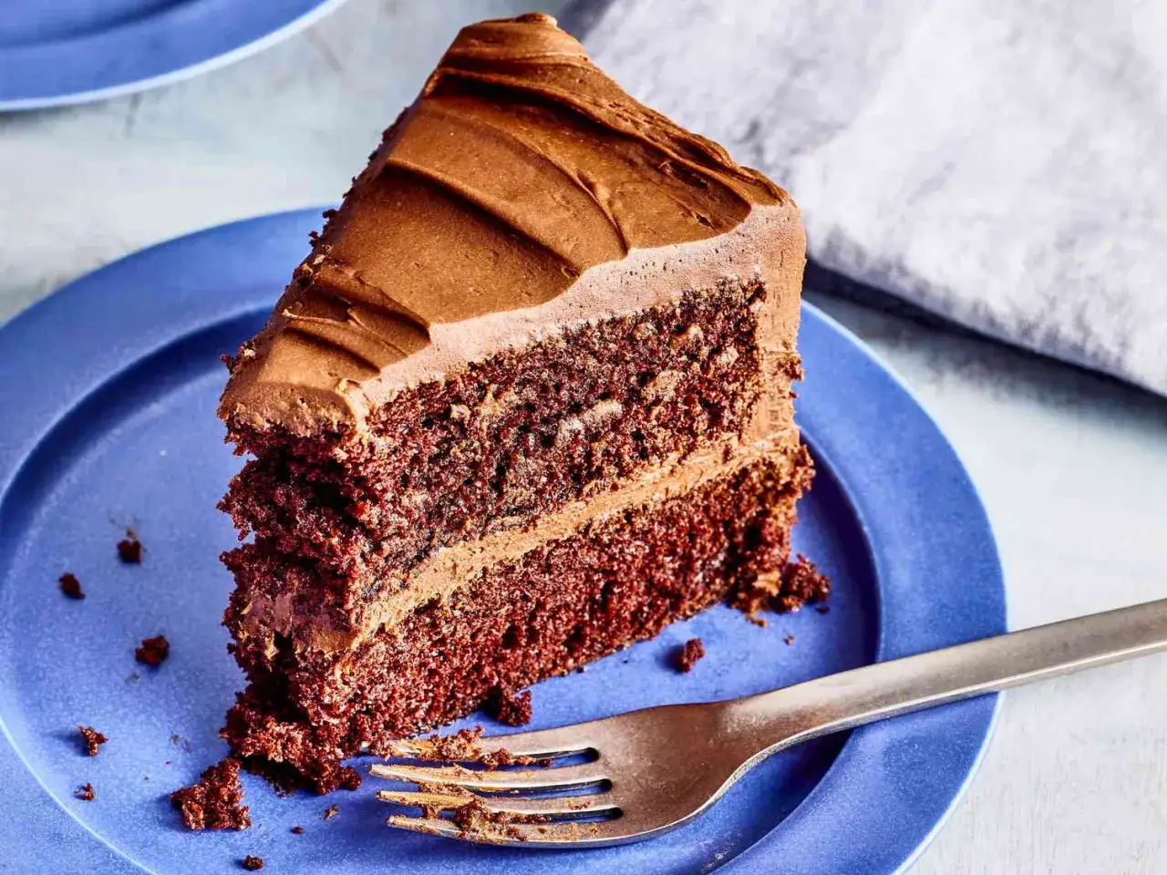 Ein saftiges Stück Schokoladenkuchen mit Schokoladenglasur auf einem blauen Teller. Dieses schokoladenkuchen rezept saftig ist ein Traum!