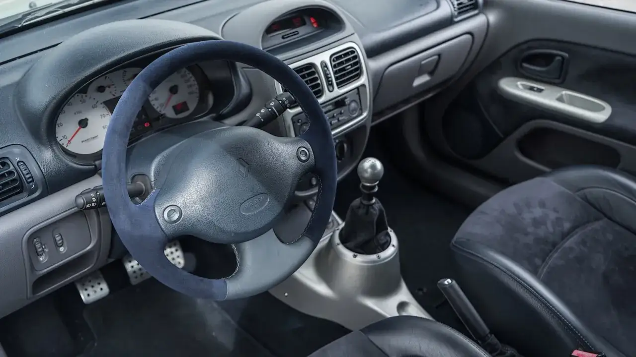 Wnętrze sportowego Renault Clio V6: kierownica obszyta alcantarą, metalowe pedały i gałka zmiany biegów.