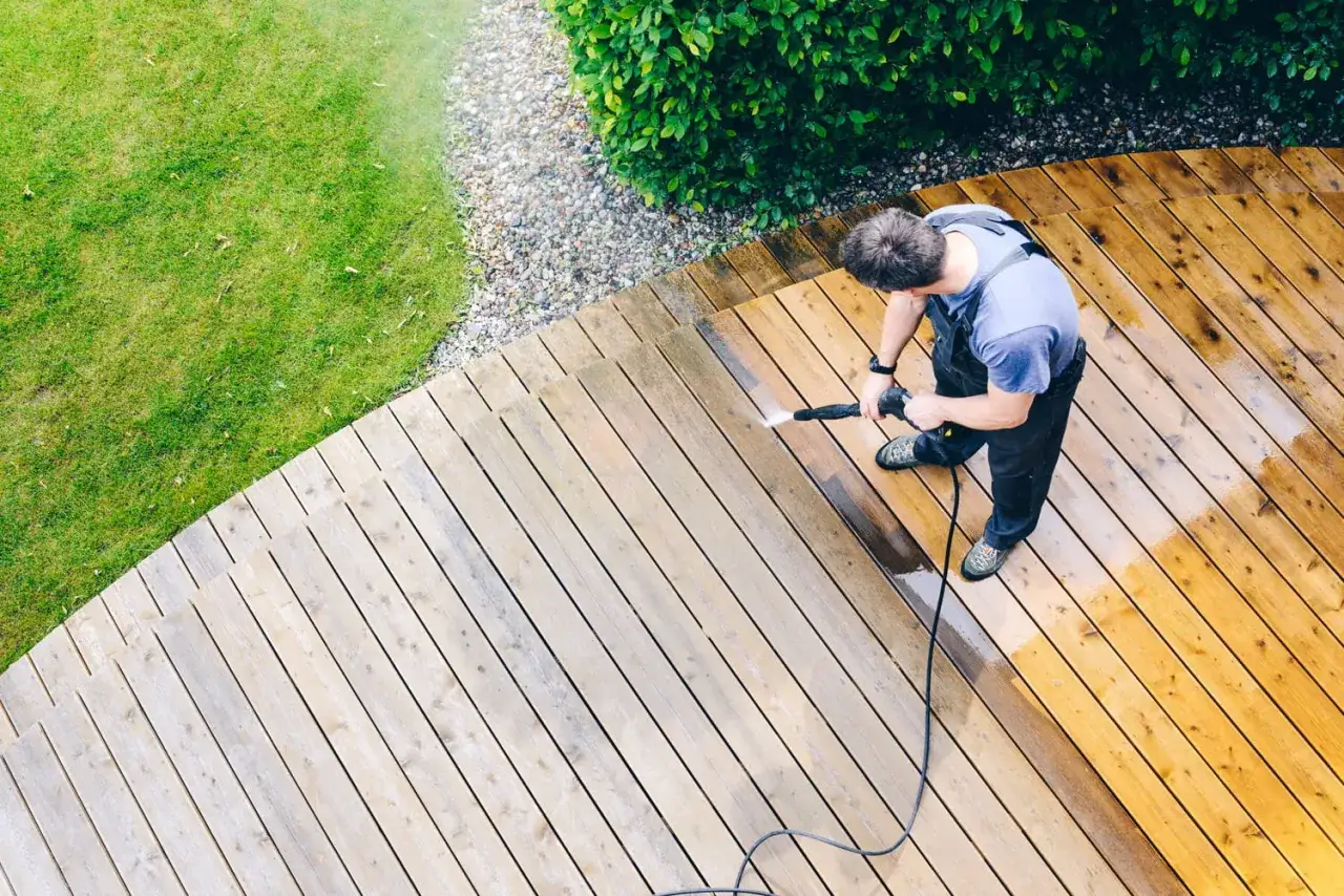 Homme nettoyant une terrasse en bois avec un nettoyeur haute pression. Il se demande combien de temps laisser agir eau de javel sur terrasse pour un r&eacute;sultat optimal.