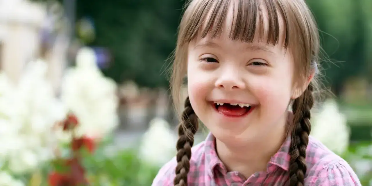 Bambina sorridente con sindrome di Down, con treccine e camicia a quadri. Un esempio di come la sindrome di Down e l'autismo non definiscano una persona.