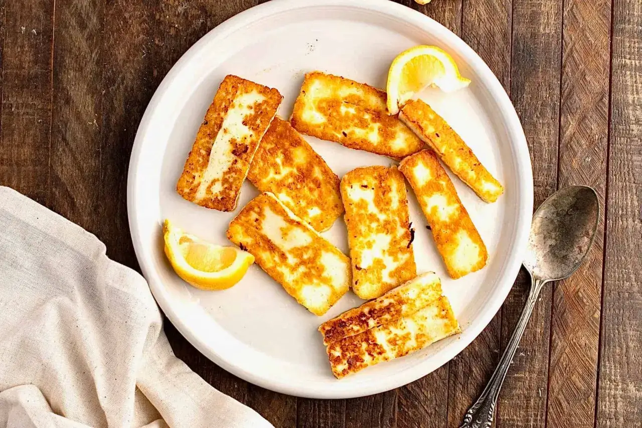 Des morceaux de halloumi grill&eacute; dor&eacute;s et savoureux, servis avec des quartiers de citron sur une assiette blanche.