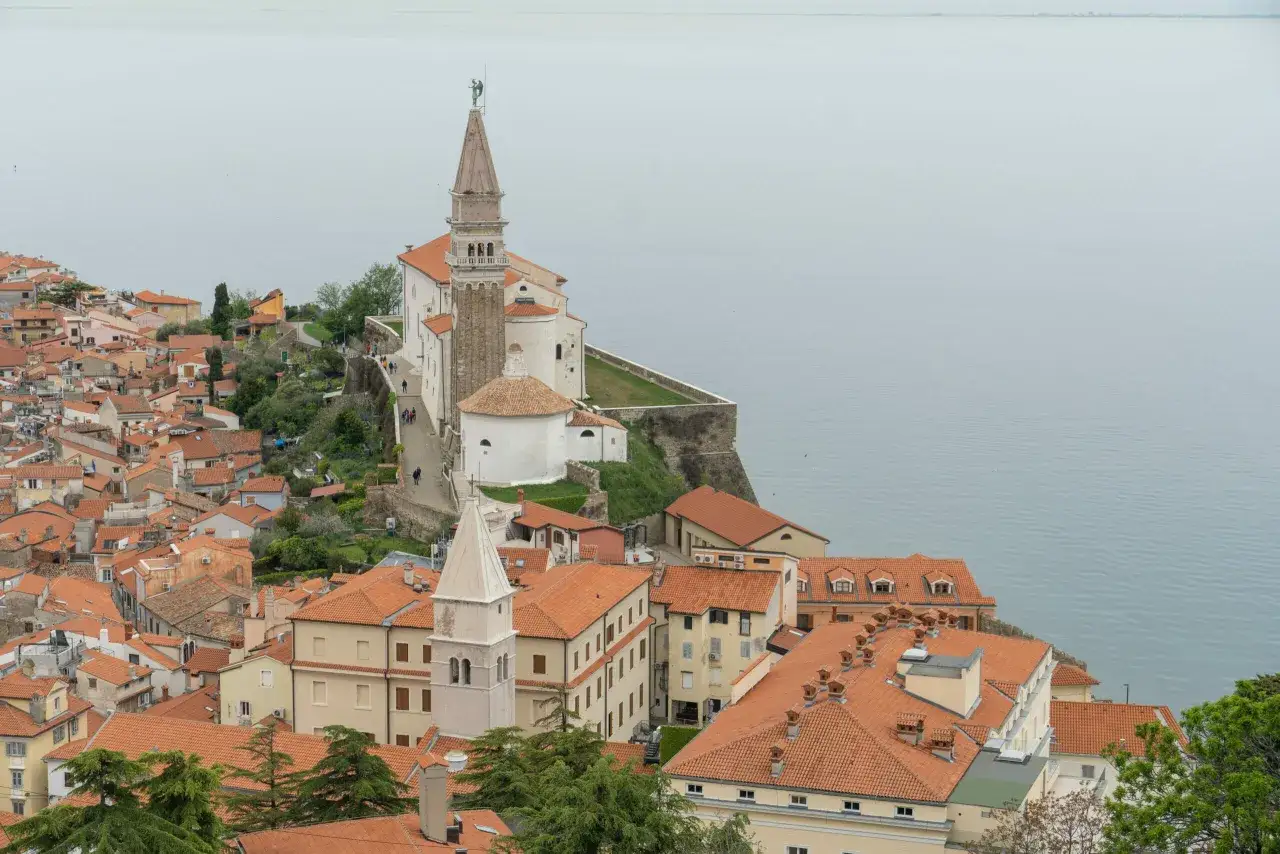 Blick über die Dächer der piran altstadt mit der Kirche St. Georg auf einem Hügel am Meer.