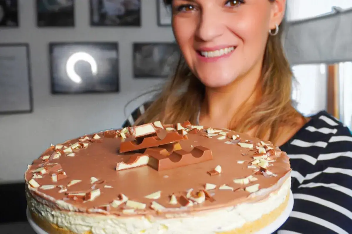 L&auml;chelnde Frau pr&auml;sentiert eine k&ouml;stliche Kinderriegel Torte, dekoriert mit Schokoriegeln und gehackter Schokolade.