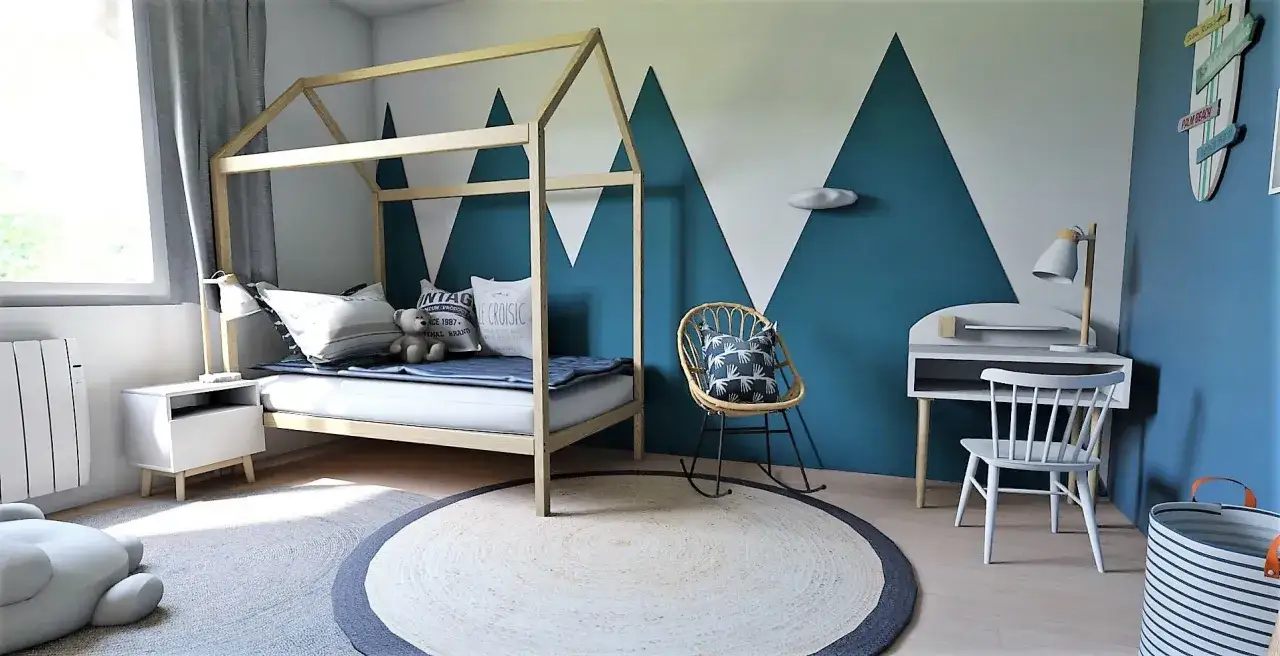 Lit cabane en bois, mur montagne bleu, fauteuil rotin, bureau enfant. Une belle idee deco lit cabane pour une chambre d'aventurier.