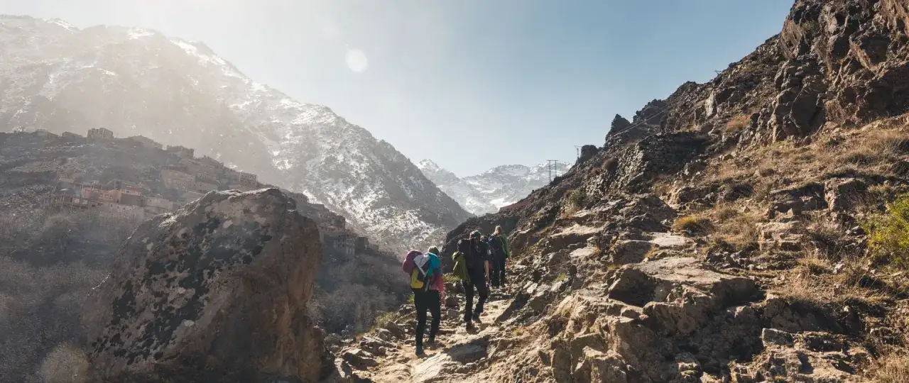 Un groupe de randonneurs s'engage sur un sentier rocailleux, dominant un village berbère accroché à flanc de montagne. Un magnifique trek Maroc.