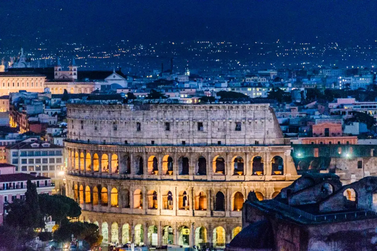 Il Colosseo illuminato di notte, un'icona da visitare a Roma, con la città sullo sfondo.