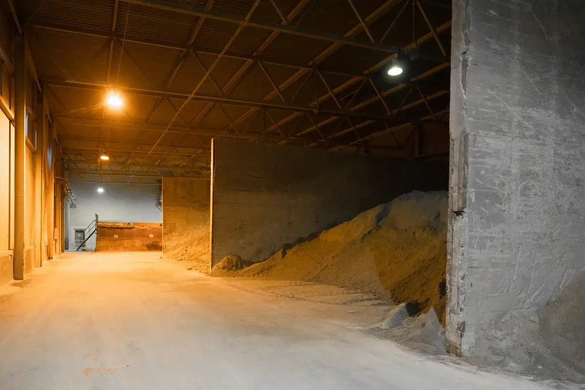 Wnętrze magazynu z hałdami materiału, być może do produkcji cerplast. Jasne oświetlenie podkreśla surowość przestrzeni.