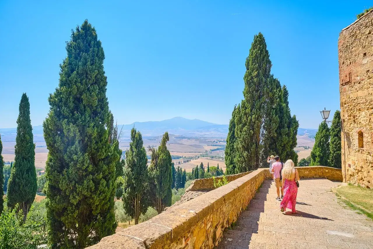 Coppia in un tour toscana 5 giorni, ammira il paesaggio collinare con cipressi e un borgo antico.