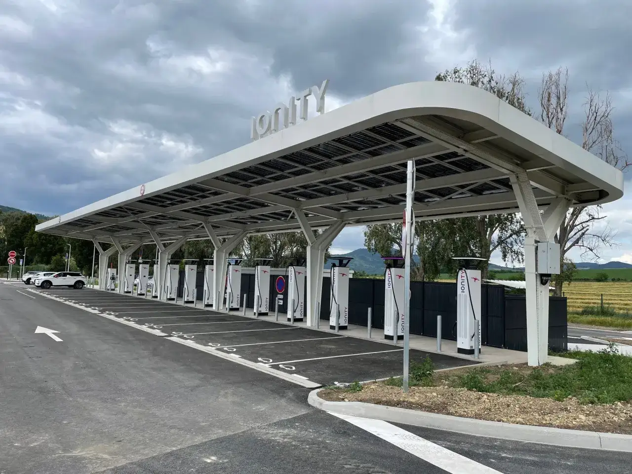 Une **ionity station de recharge** moderne avec plusieurs bornes de recharge rapides sous un auvent couvert de panneaux solaires.