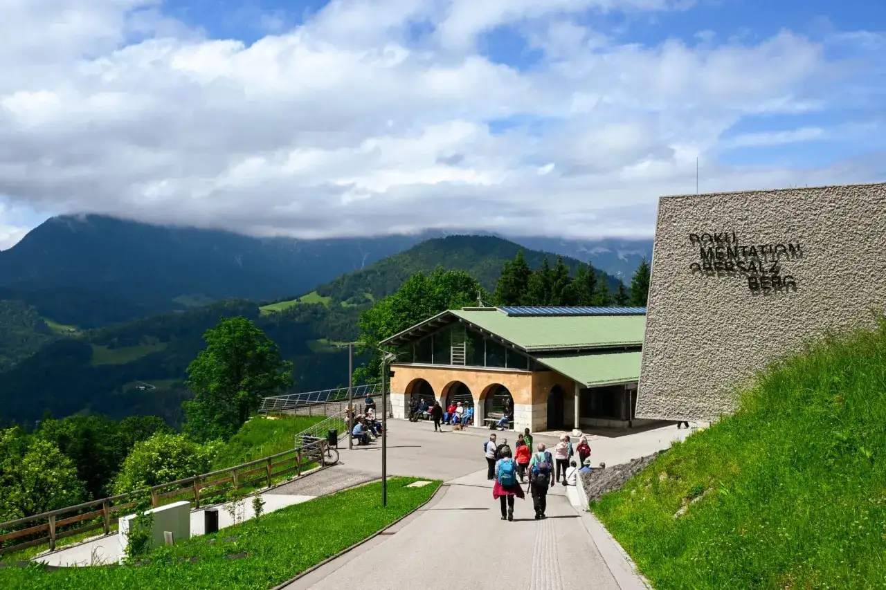 Besucher erkunden das Dokumentationszentrum Obersalzberg, umgeben von grünen Hügeln und Bergen.