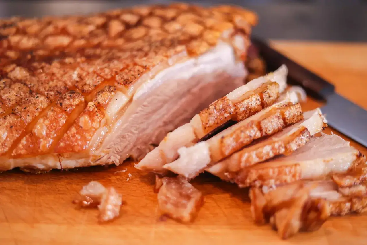 Un d&eacute;licieux lard r&ocirc;ti au four, croustillant et juteux, est tranch&eacute; sur une planche en bois.