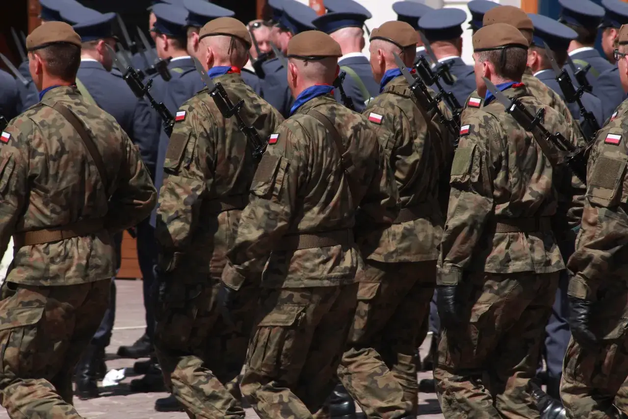 Żołnierze w mundurach moro, z karabinami i bagnetami, prezentują swoje wojskowe uposażenie.