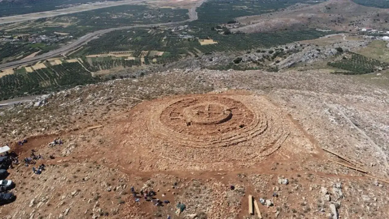 Vue aérienne d'un site archéologique circulaire, rappelant un labyrinthe où un minotaure pourrait se cacher. Des archéologues travaillent sur le site.