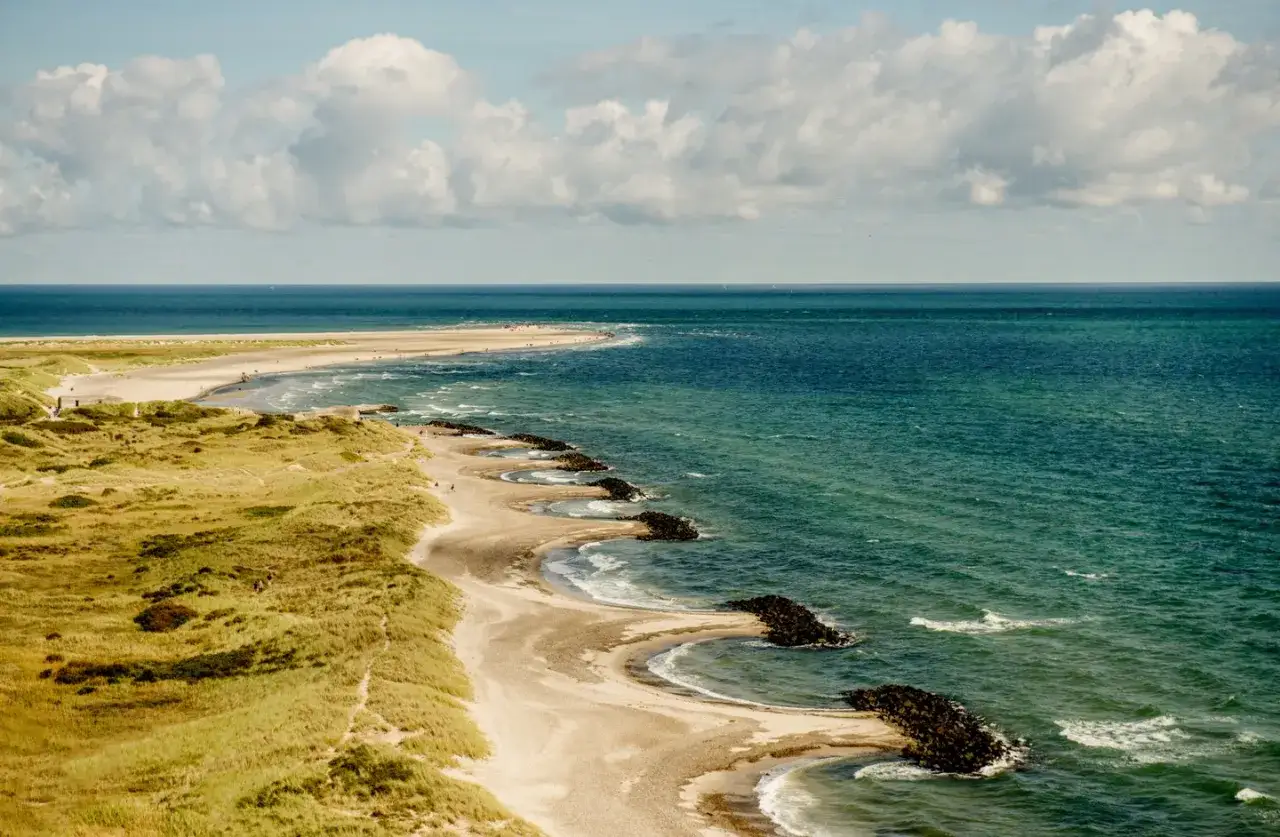 En vidstr&auml;ckt kustlinje med sanddyner, gr&auml;s och det turkosa havet. En vacker vy &ouml;ver danmark natur.