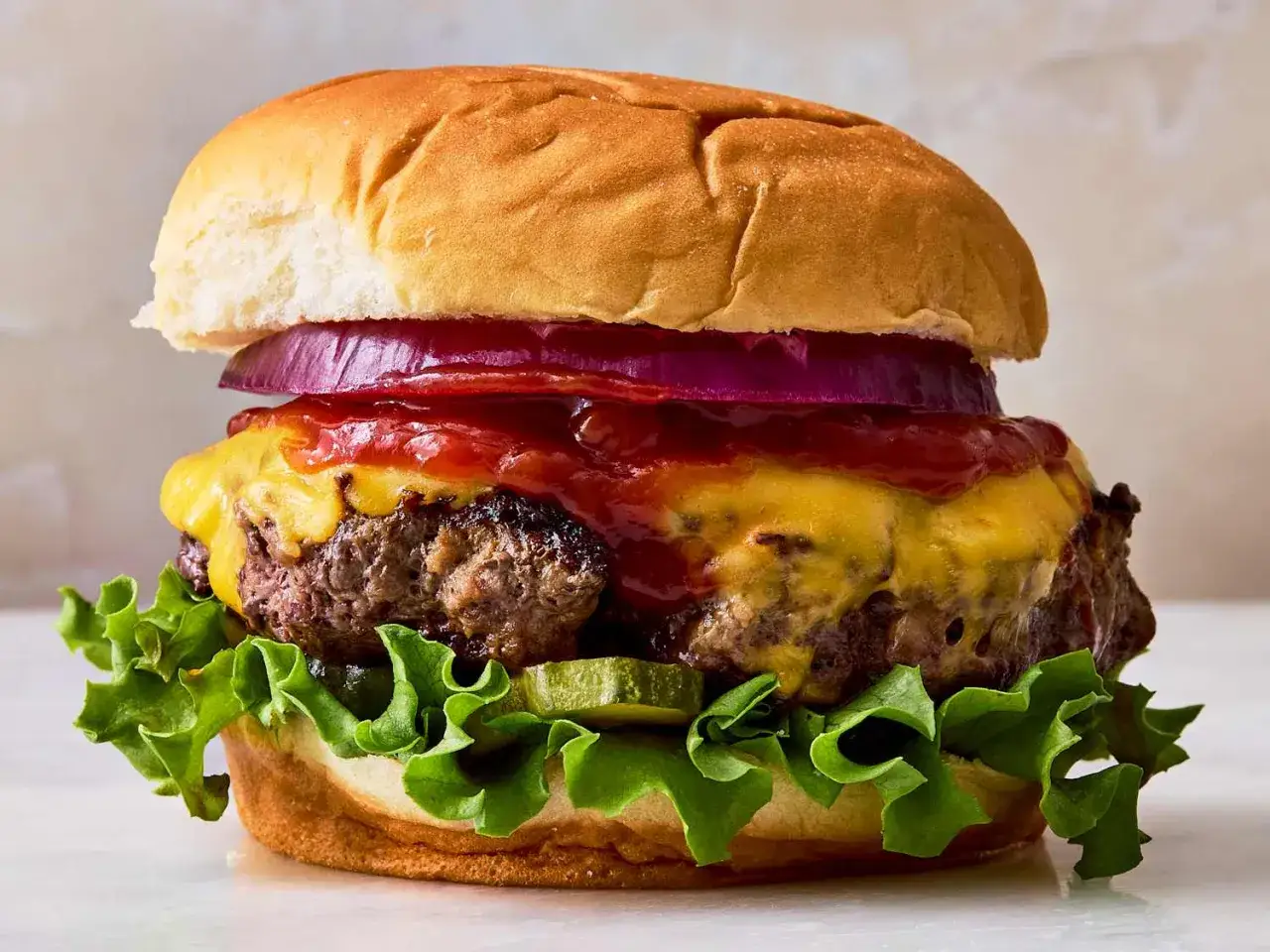 Un délicieux burger maison avec steak juteux, fromage fondant, oignons rouges, cornichons et laitue croquante. Une recette parfaite pour un repas gourmand.