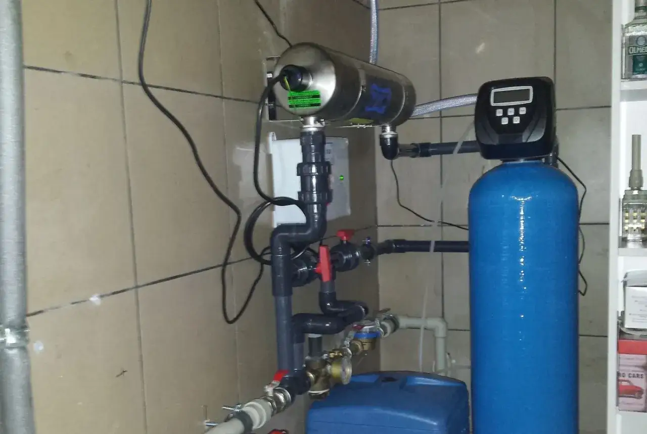 Montaż stacji uzdatniania wody: niebieski zbiornik, lampa UV, zawory i rury tworzą system oczyszczania.