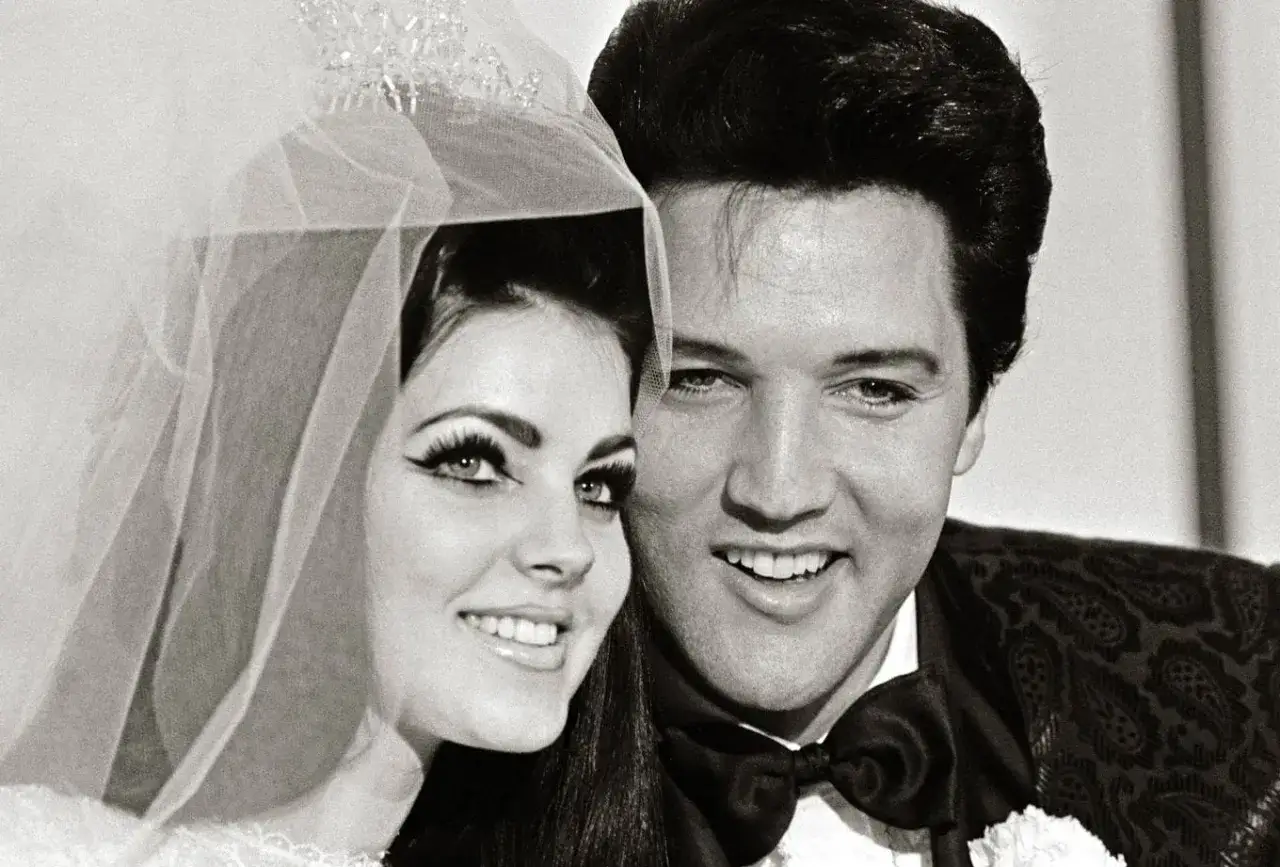 Priscilla Presley im Brautkleid, mit Schleier und Tiara, l&auml;chelt neben Elvis Presley, der einen Smoking tr&auml;gt. Ein ikonisches Bild von Priscilla Presley 70s.