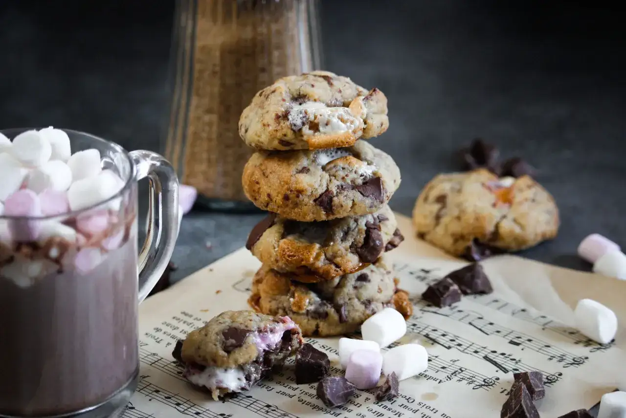 Un cookie chamallow fondant, empil&eacute; avec d'autres, &agrave; c&ocirc;t&eacute; d'une tasse de chocolat chaud garnie de guimauves.