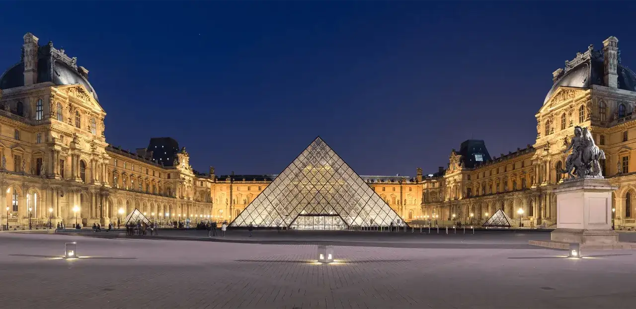 Louvren i Paris upplyst på natten med sin ikoniska glaspyramid. Här finns fakta om Louvren.