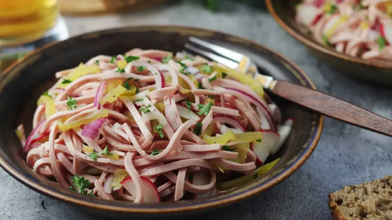 Bayerischer Wurstsalat, frisch zubereitet mit Wurststreifen, Zwiebeln, Radieschen und Petersilie, serviert in einer rustikalen Schüssel.