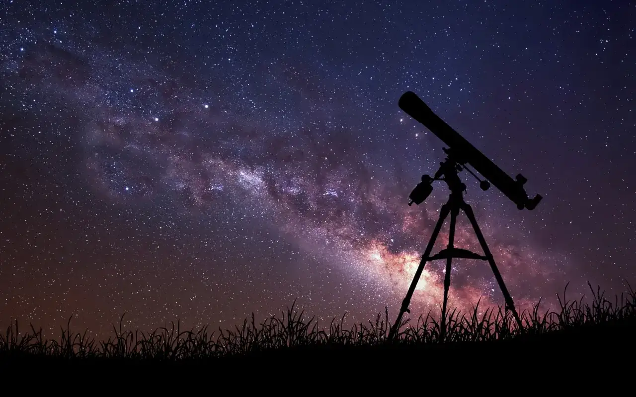 Télescope pointé vers la Voie lactée, silhouette d'herbes au premier plan. On dirait que quelqu'un a une bonne étoile pour observer le cosmos.