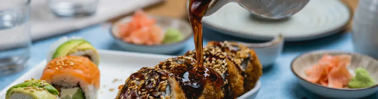 Polewany sosem do chińszczyzny, chrupiący rolka sushi z sezamem. Obok sushi z łososiem i awokado, imbir i wasabi.