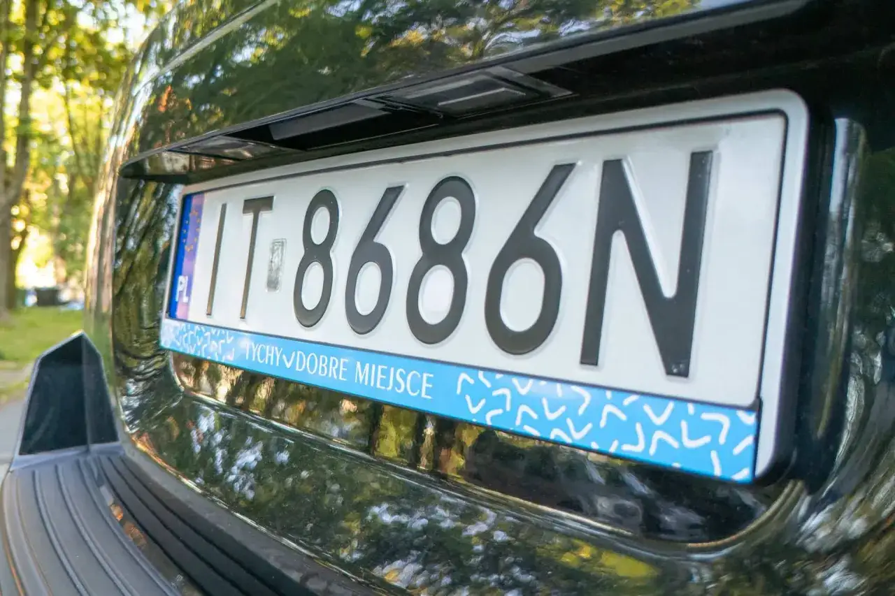Tablica rejestracyjna IT 8686N na czarnym samochodzie. Pod nią niebieski pasek z napisem 