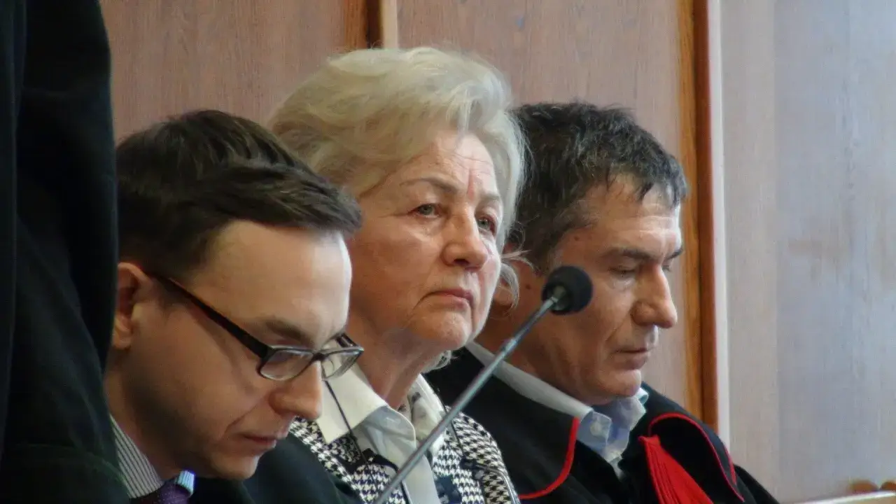 Trzy osoby w togach sądowych. W środku starsza kobieta, po jej bokach mężczyźni. Może to być fragment z życiorysu Jerzego Ziobry.