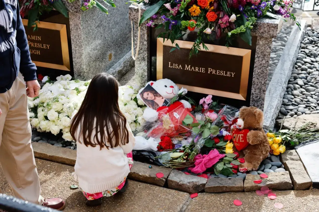 Dziecko klęczy przy grobie Lisy Marie Presley, obok kwiatów i pluszowych misiów. Pamięć o Benjaminie Keough trwa.