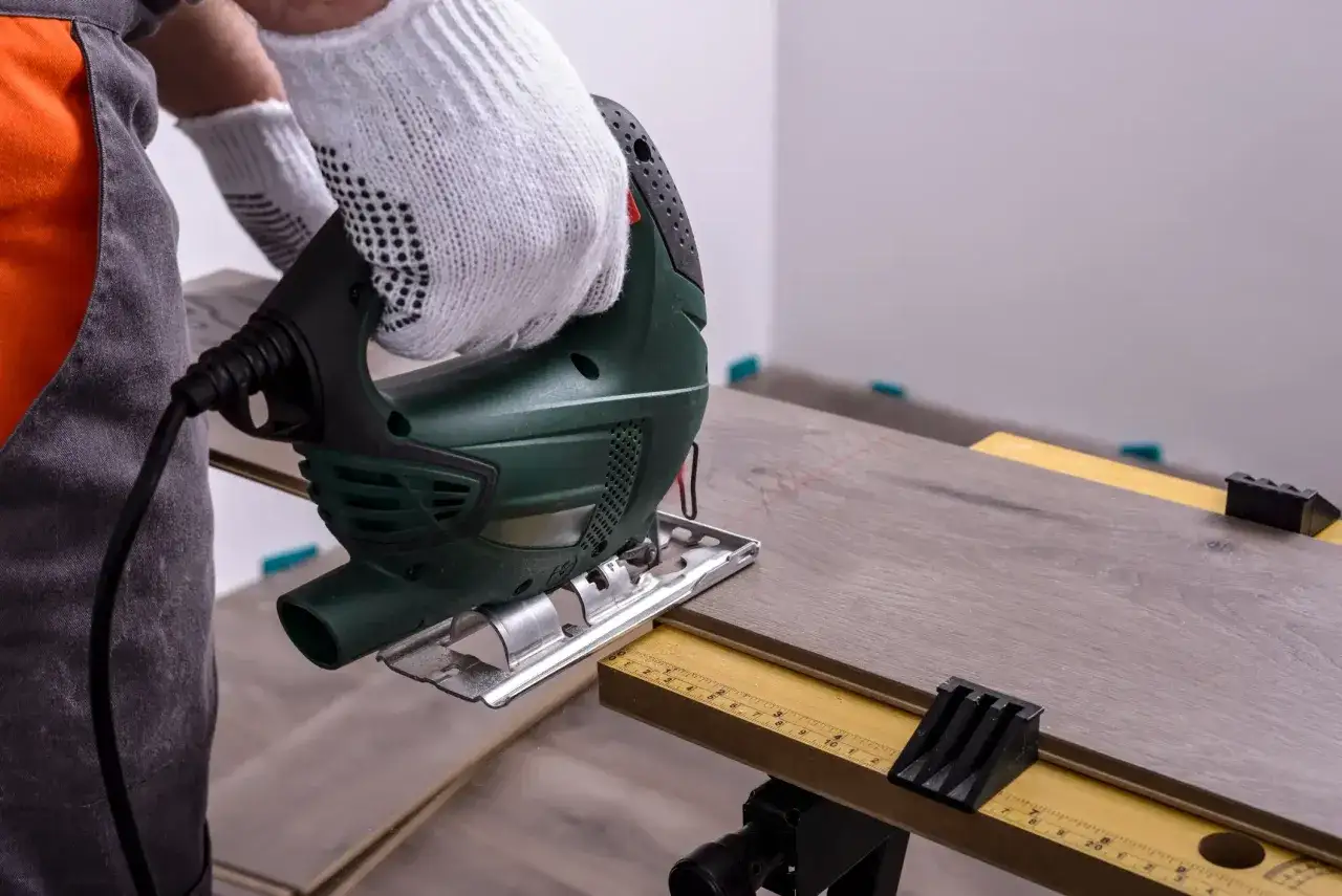 Mit einem Stichs&auml;ge wird Laminat schneiden. Ein Handwerker mit Handschuhen arbeitet pr&auml;zise.