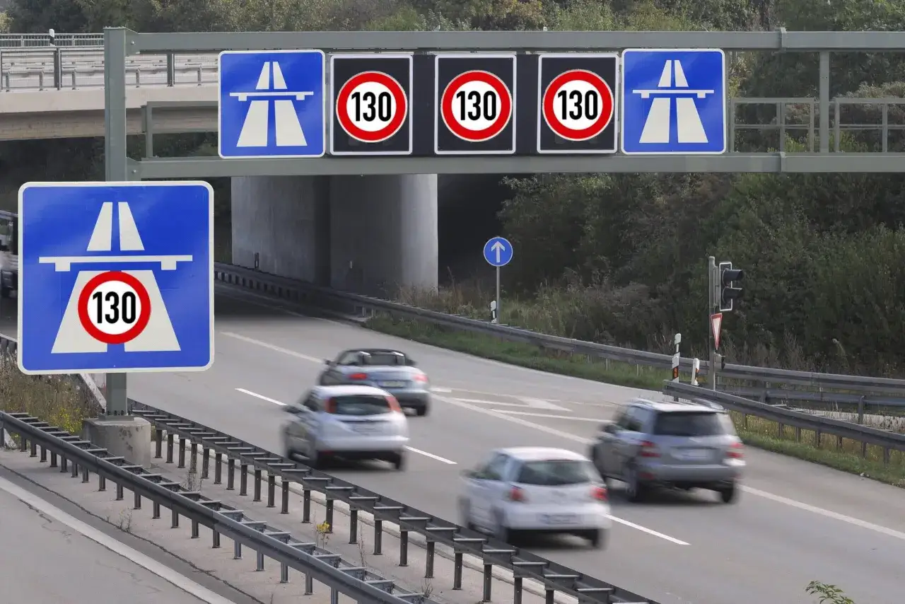 Segnali di limite velocità autostrada 130. Auto in transito su strada a più corsie, con cartelli blu che indicano l'autostrada e segnali circolari rossi con il numero 130.