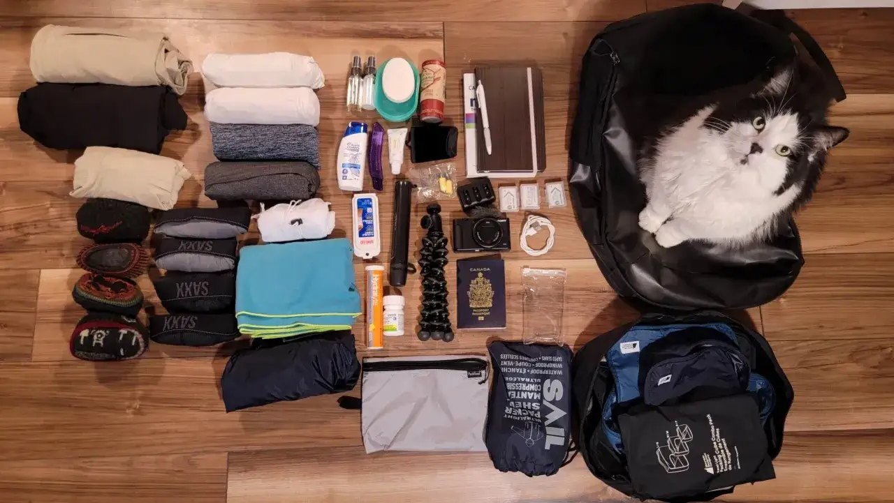 Neuseeland Kleidung und Reiseutensilien sind bereit f&uuml;r das Abenteuer. Ein flauschiger Reisebegleiter wacht &uuml;ber den Rucksack.