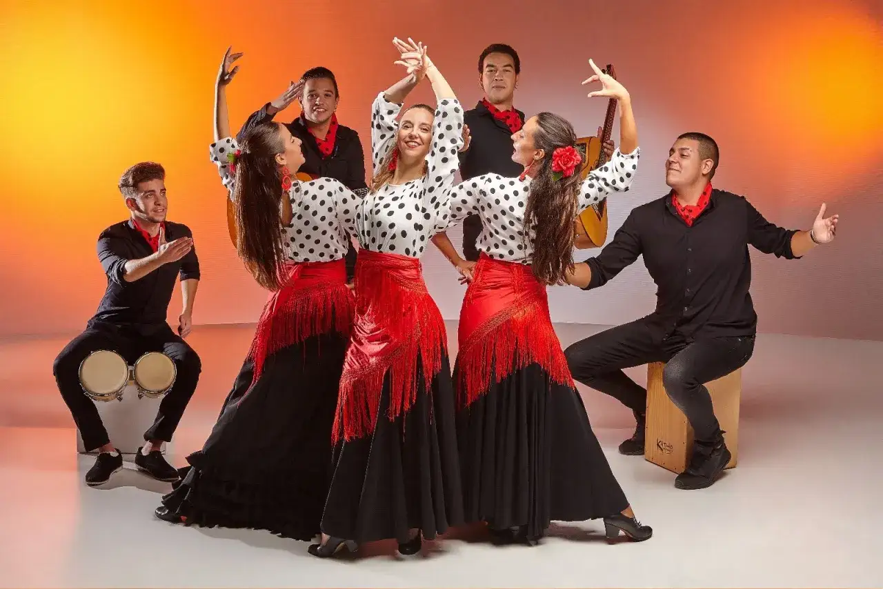 Grupo de bailarines y músicos interpretando rumba catalana actual. Mujeres con faldas rojas y blusas de lunares, hombres tocando percusión y guitarra.