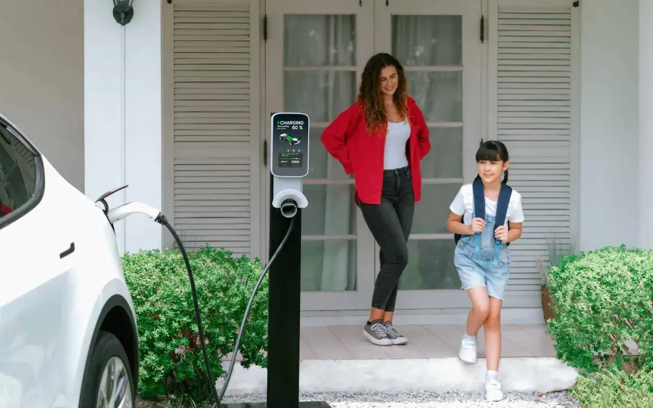 Madre e hija salen de casa mientras el coche el&eacute;ctrico est&aacute; en **tiempo de carga**. La estaci&oacute;n de carga muestra 60%.