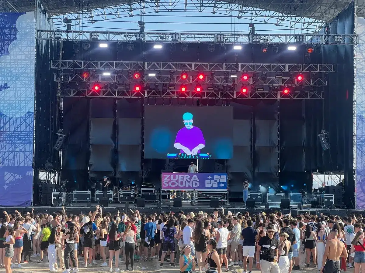 Multitud disfrutando de un concierto al aire libre con el logo de zuera sound en la pantalla.