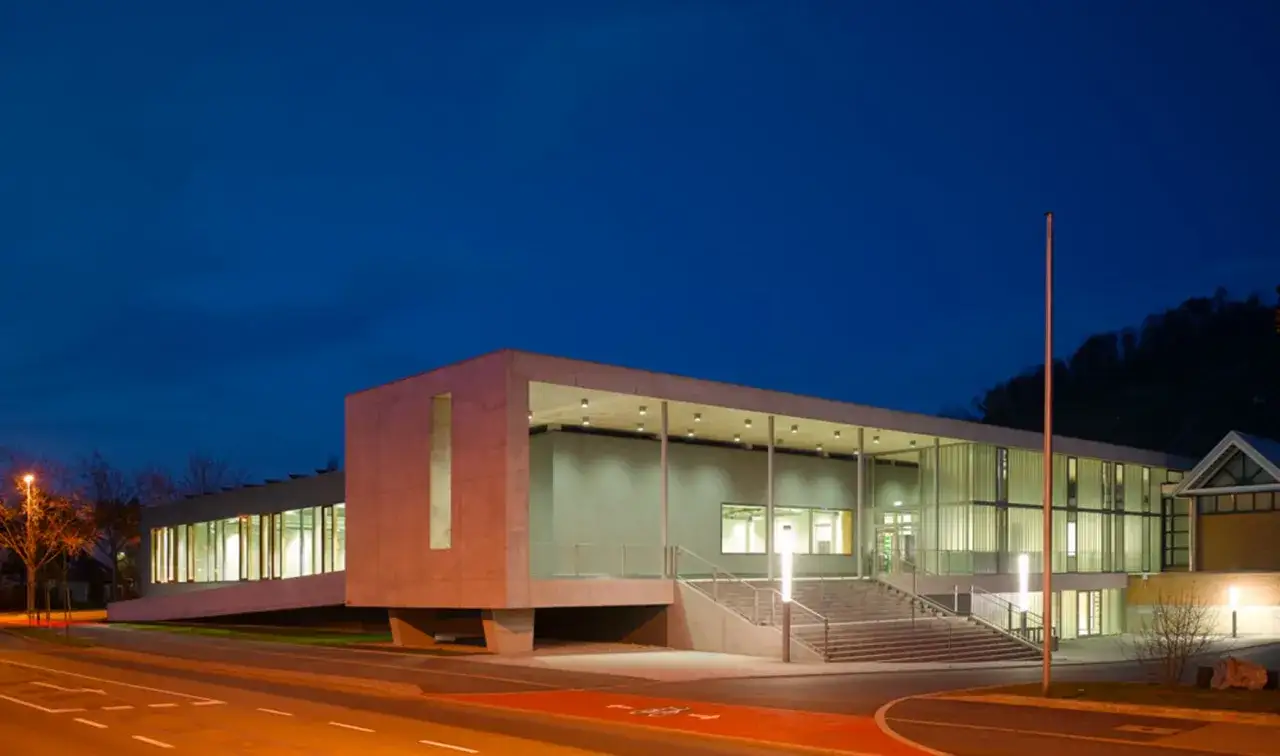 Moderne Stadthalle Metzingen im Abendlicht, mit Betonfassade und Glasfront, beleuchtete Fenster und Treppenaufgang.