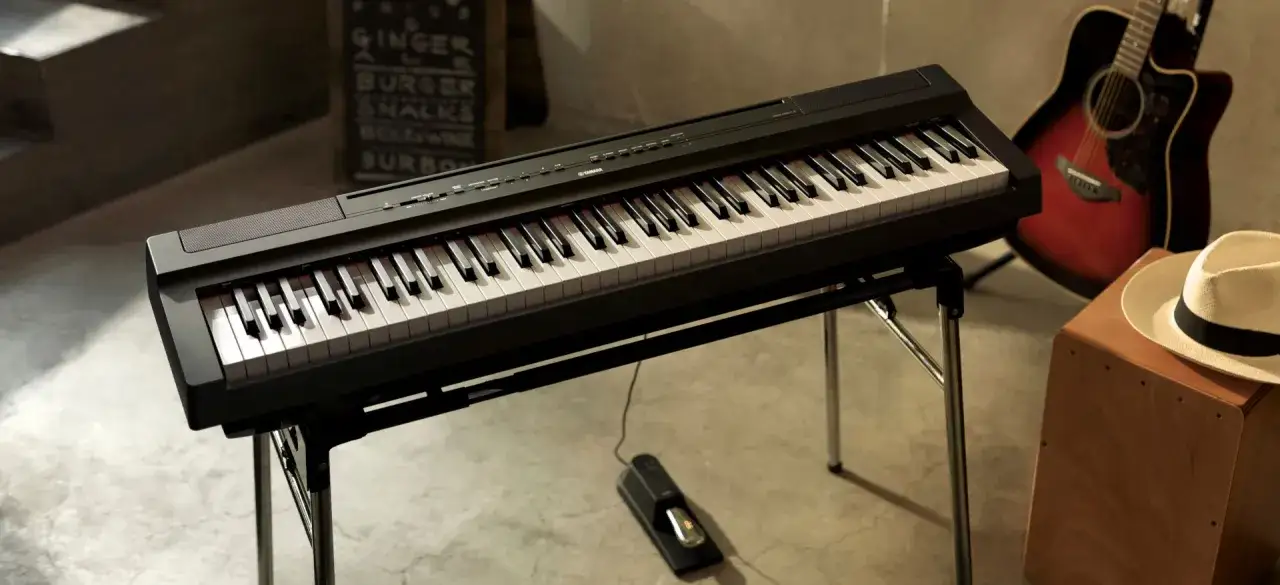 Un piano num&eacute;rique noir sur un stand, pr&ecirc;t &agrave; jouer. Une guitare acoustique et un chapeau compl&egrave;tent la sc&egrave;ne musicale.