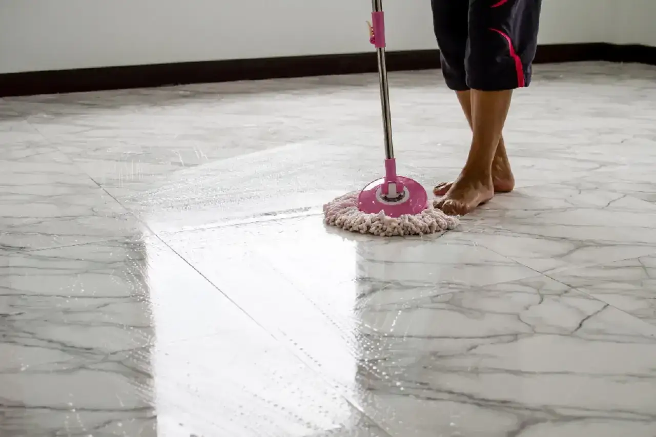 Una persona pulisce un pavimento in marmo con uno straccio, usando una soluzione che potrebbe contenere bicarbonato per pavimenti per una pulizia profonda.