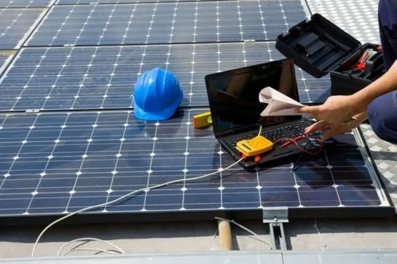 Technicien effectuant la reparation panneau solaire avec un ordinateur portable, un multimètre et un casque bleu sur les panneaux.