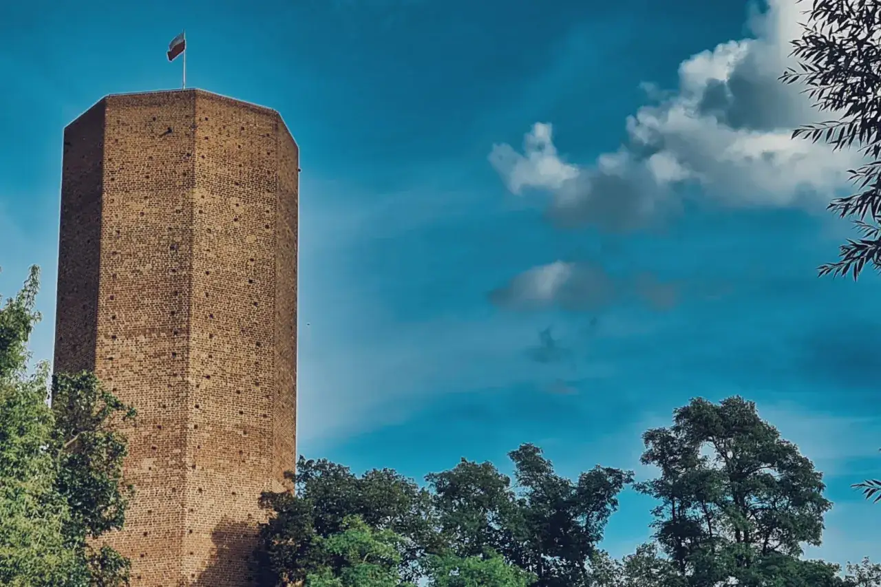 Wieża z polską flagą, niczym z baśni o Popielu, góruje nad zielonymi drzewami.