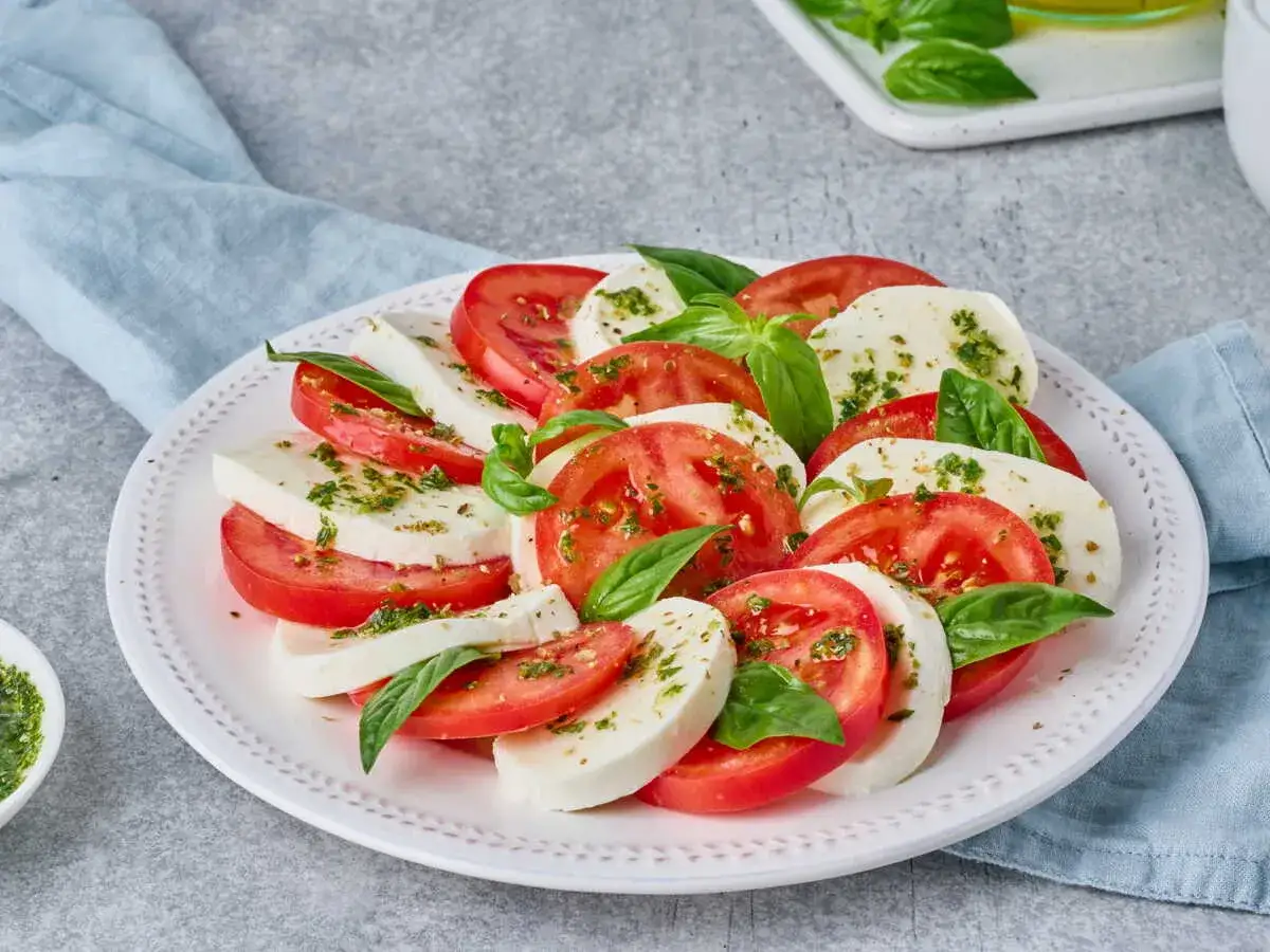 Une salade de tomates et mozzarella, garnie de basilic frais et d'herbes. Un délice estival simple et coloré.