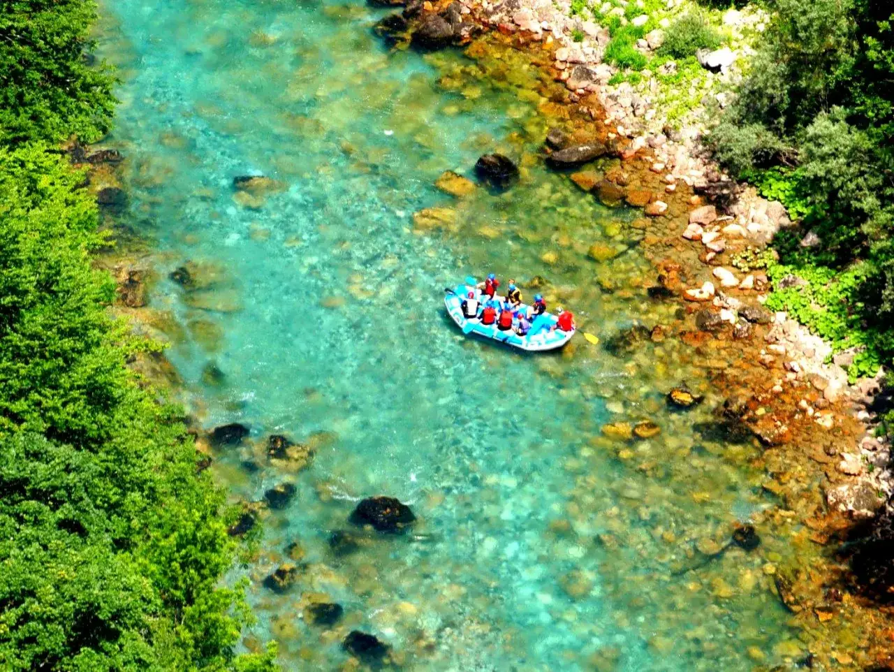 Rafting na turkusowej rzece w kanionie rzeki Tara. Grupa turyst&oacute;w w kamizelkach ratunkowych płynie pontonem po krystalicznie czystej wodzie.