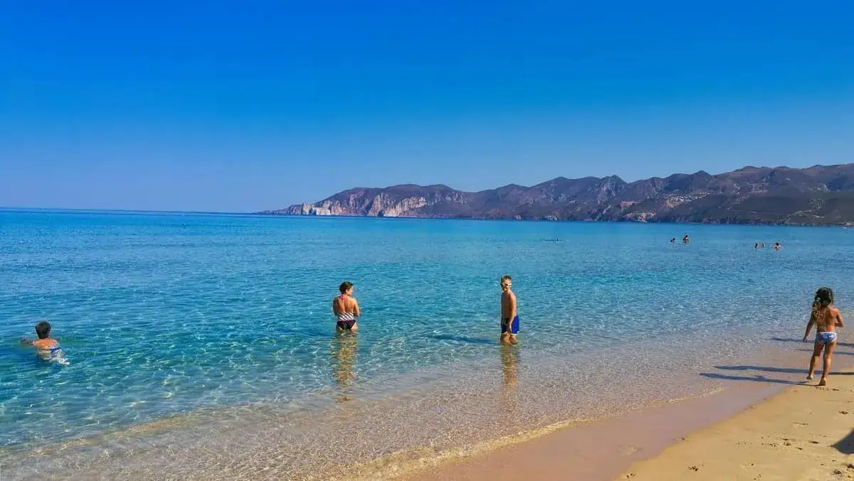 Niños disfrutan de las aguas cristalinas de Cerdeña, con montañas al fondo.